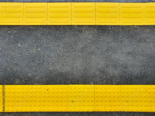 Yellow tactile paving safety warning lines on a dark asphalt train station platform.