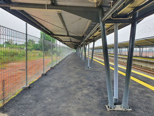 Long empty outdoor train station platform with a covered walkway and tracks.