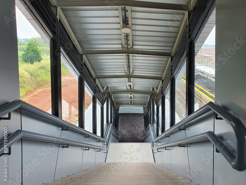 Descending stairs inside a modern metal and glass pedestrian footbridge.