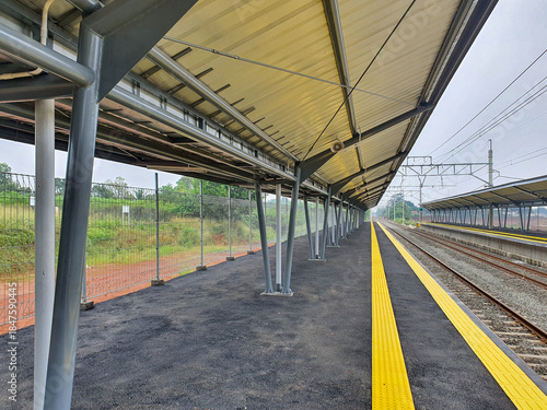 Empty train station platform with yellow safety line next to railway tracks.