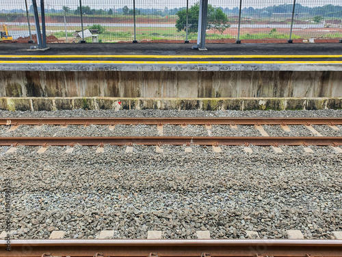 View of empty railway tracks from a station platform looking out towards a rural landscape.