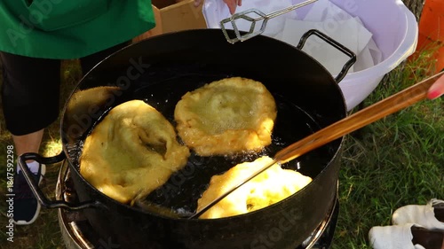Traditionally way of cooking, frying dough in oil or pork fats making delicious treat in a large rustic pot, deep iron cauldron over open fire.