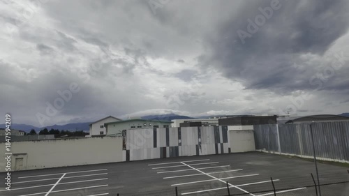The train passes a row of neat factory buildings under heavy, dark clouds.