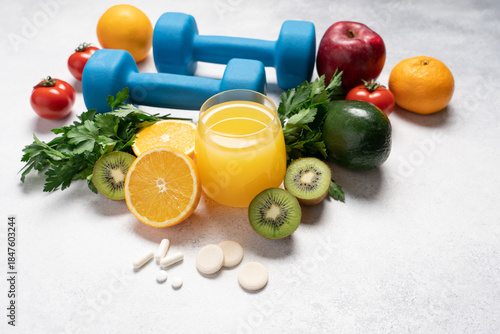 Youth and Health Preservation Concept with Vitamins, Dumbbells, Fresh Vegetables, Fruits, Greens and Orange Juice on Light Background