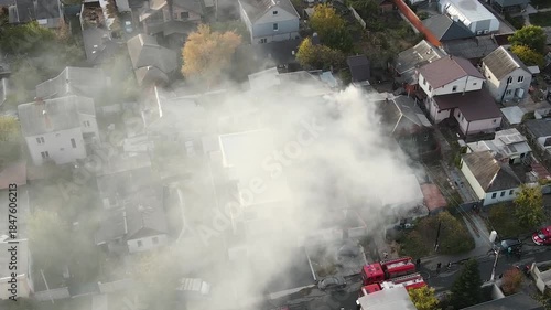 A fire in a private residential area: thick white smoke rises from the roofs of private homes. Aerial (drone) view of the scene. Fire rescue operations: on the charred roof, the remains of the fire.