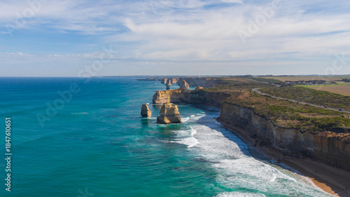 Aerial view of majestic limestone stacks meet the turquoise ocean under a vast sky along the Twelve Apostles coastline, Twelve Apostles, Victoria, Australia.
