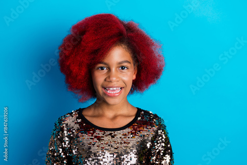 Happy young girl with red dyed hair wearing a sequined top against a bright blue background
