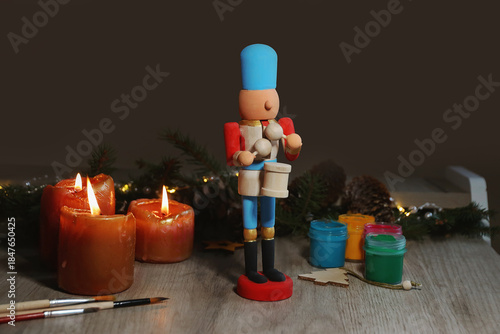 Wooden toy fairytale Nutcracker painted with colors, spruce branches, pinecones and candles on table on dark background