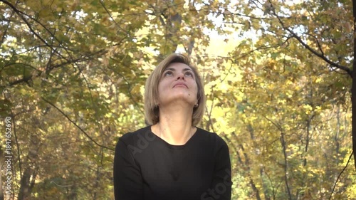 A joyful woman throws vibrant golden autumn leaves into the air in a sunlit park. Capturing the essence of fall, freedom, and seasonal beauty.
