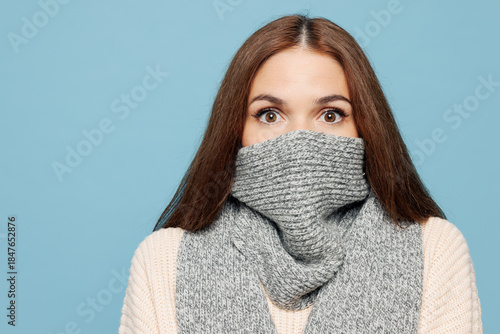 Obraz na płótnie Close up young shocked scared woman wear pink sweater cover mouth with grey scarf isolated on plain blue background studio portrait