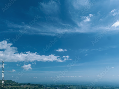 Beautiful aerial view of terraced vegetable plantations on a lush mountain slope under a bright blue sky with white clouds.