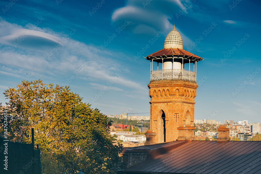 Fototapeta premium Brick minaret featuring a domed top of central Mosque in Tbilisi, rising above a building roof under a blue sky