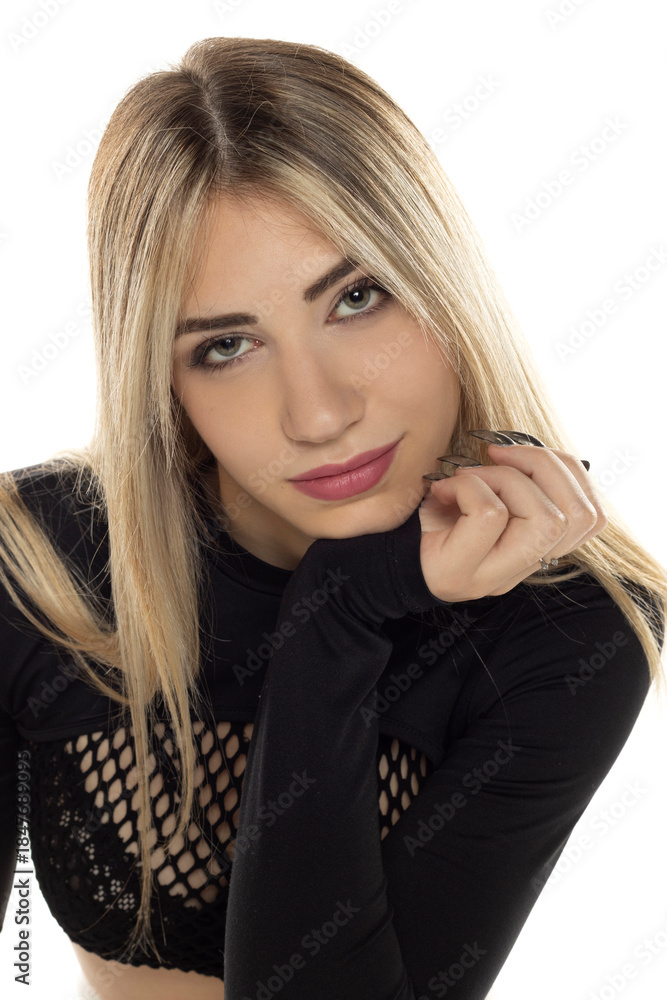 Naklejka premium Studio portrait of blonde woman in black long sleeve crop top with relaxed expression resting her chin on hand on white background