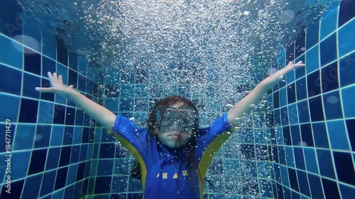 Kid dropping into swimming pool with bubbles surrounding in slow motion
