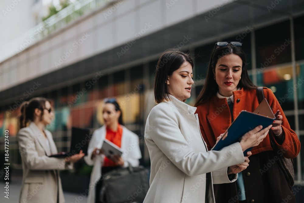 Obraz premium Associates stand outside a contemporary office, discussing a blue folder and notes. They wear stylish coats and sunglasses, conveying collaboration, planning, and friendly energy in an urban setting.