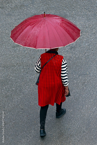 back view of a woman with red umbrella walking on wet asphalt road