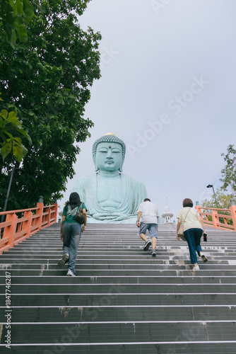 People ascending a wide staircase towards the Great Buddha monument at a Thai temple