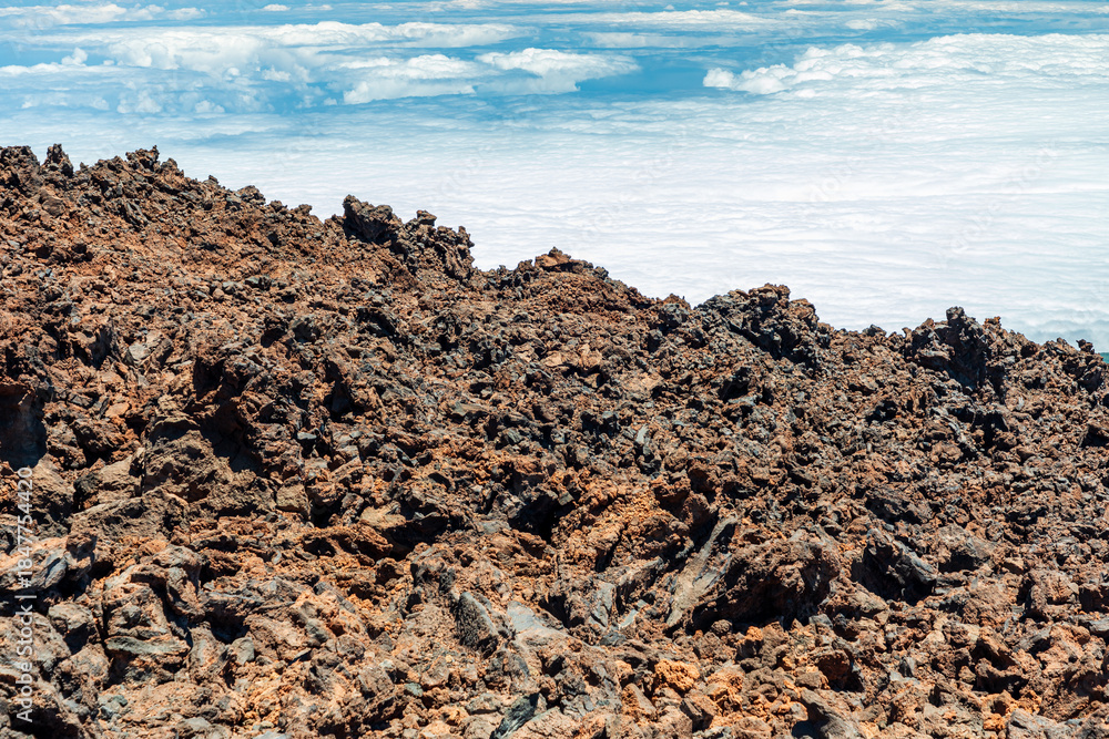 Obraz premium Rugged lava rocks meet blue sky and white clouds in a desolate coastal landscape