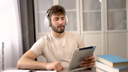 A young man wearing headphones, watching something on his laptop in a relaxed home environment.