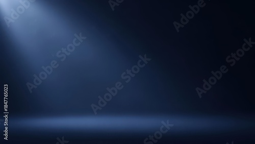 Empty dark blue studio stage illuminated by a single powerful spotlight beam from above, creating a dramatic and moody atmospheric background for product display.