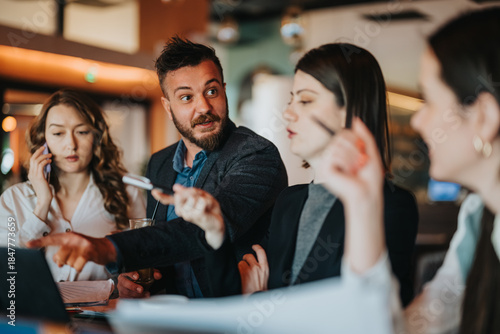 A group of colleagues and coworkers sit around a table in a cafe-like office space, sharing ideas, negotiating, and planning a project.