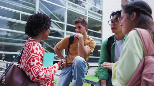 Diverse students chat by a modern glass building on campus, one checking a smartphone while friends listen. Casual after-class moment highlighting study life and teamwork.