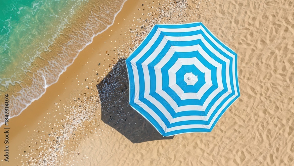 Naklejka premium Aerial view of blue and white striped umbrella on sandy beach with turquoise waves