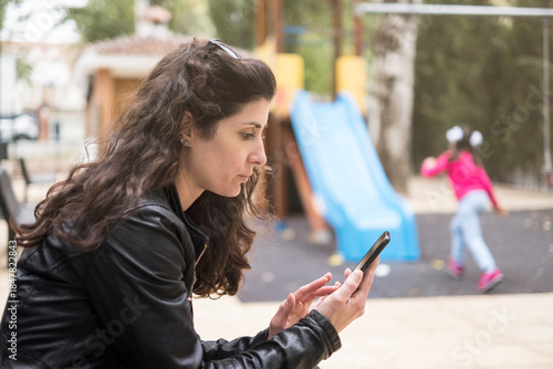 Distracted mother with the phone while daughter plays on the slide