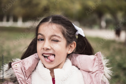 Little pretty girl looking at camera in park winter scene, tongue out