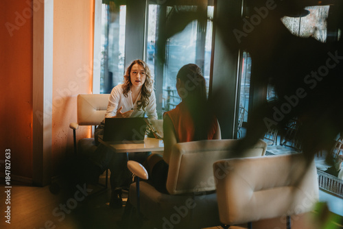 Quadro em tela Two colleagues exchange ideas in a cafe setting, with a laptop on the table and warm natural light