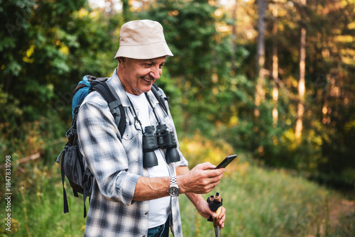 Wallpaper Mural Portrait of smiling senior hiker with backpack and binoculars using smartphone while discovering nature during solo mountain hike. Torontodigital.ca