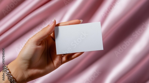 Elegant hand holding blank card on luxurious pink satin background for branding mockup
