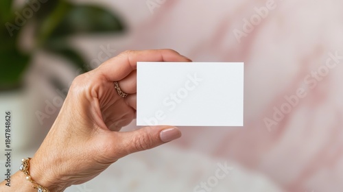 Hand holding blank business card against soft pink background for mockup design