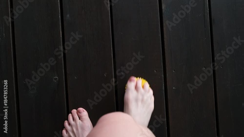 Female feet are doing foot exercises by rolling a prickly massage yellow ball under the foot on the floor pressing down in different sides. Training to correct and relax the foot fascia. 4k footage.