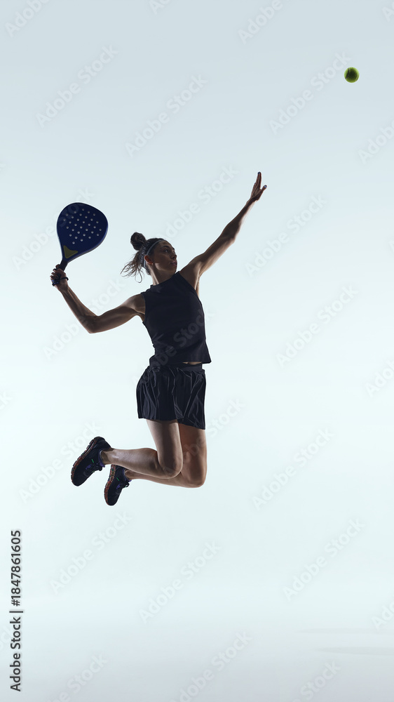 Naklejka premium Female padel player jumping for powerful overhead shot on white background. Concept of professional padel sport, athletic performance, competitive training, modern racket sport advertising.