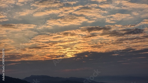 Sunrise over the mountains, painted in hues of orange, pink, and gold, with soft clouds drifting across the sky in a breathtaking natural display