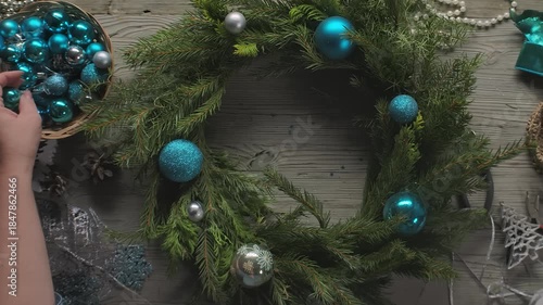 Top view panorama of female designer hands trying various ornaments on a willow and fir Christmas wreath base. DIY holiday craft and New Year preparation