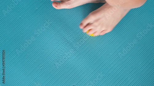 Female feet are doing foot exercises by rolling a prickly massage yellow ball under the foot on the yoga mat pressing down in different sides. Training to correct and relax the foot fascia. 4k footage