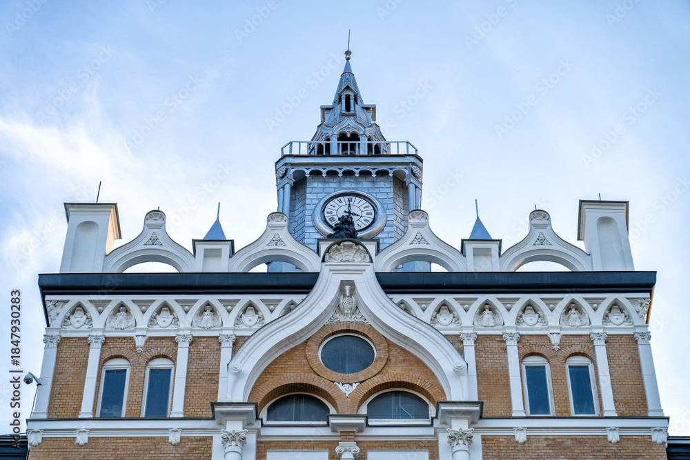 Fototapeta premium Elaborate Gothic Revival style clock tower with ornate architectural details, including arched windows, decorative friezes, and prominent clock face, against clear sky