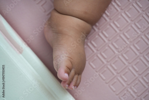 Close-up of a chubby baby's foot resting on a light pink playmat with a geometric textured pattern. Represents innocence, infancy, and soft, delicate skin.