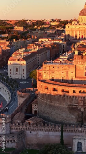 vertical video: orbiting drone shot of river Tiber and Castel Sant Angelo in Italian capital Rome at sunrise, historic Roman architecture, aerial view of Sant Angelo bridge, travel in Rome.