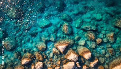 Aerial view of clear turquoise water revealing numerous submerged rocks and pebbles.
