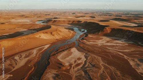 Fototapeta Naklejka Na Ścianę i Meble -  Aerial view of a winding river cutting through a vast desert landscape with sand dunes and arid terrain