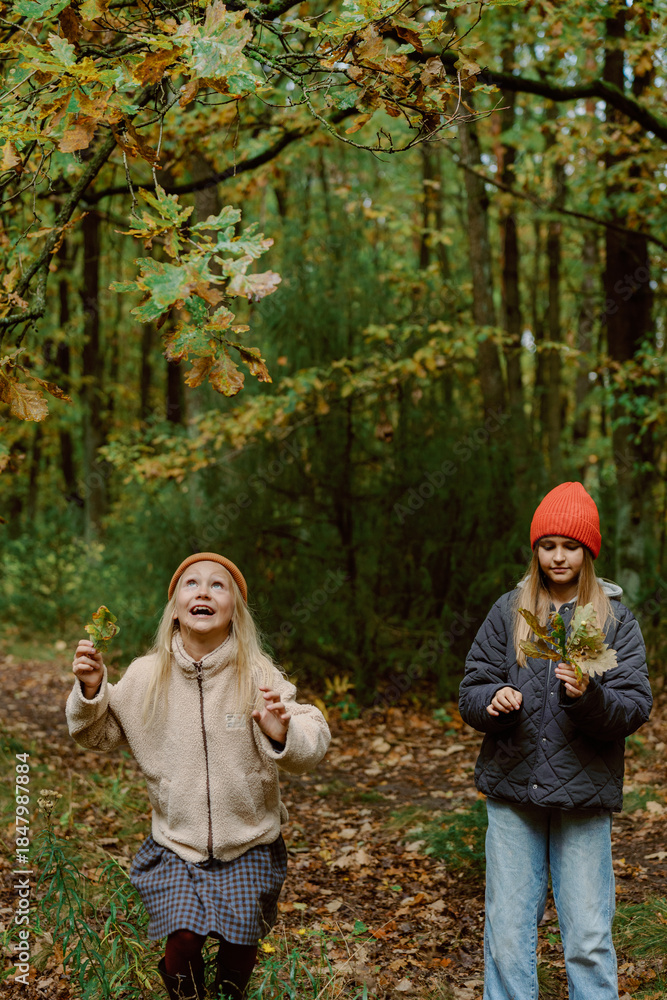 Fototapeta premium Two children enjoy a wonderful afternoon in a colorful autumn forest, surrounded by golden leaves. They laugh and collect leaves, embracing the beauty of nature.