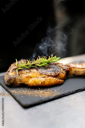 Fotografi A sizzling steak is presented on a black slate board, topped with a sprig of fre