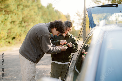 Foto Two young men focus on fixing something on a car by the roadside
