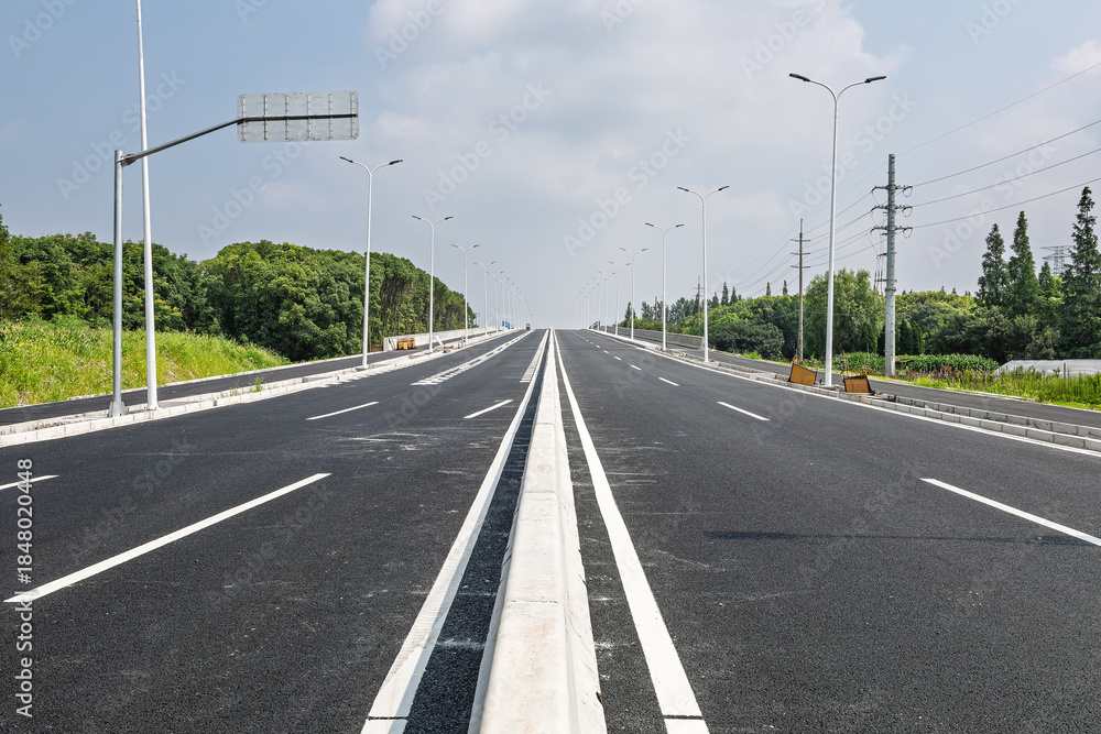 Fototapeta premium Empty newly paved asphalt road stretching into the distance under a clear sky.