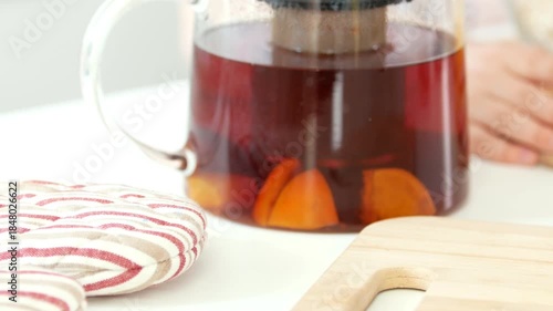 Teapot with fruit tea in front of hands of girl preparing cooking
