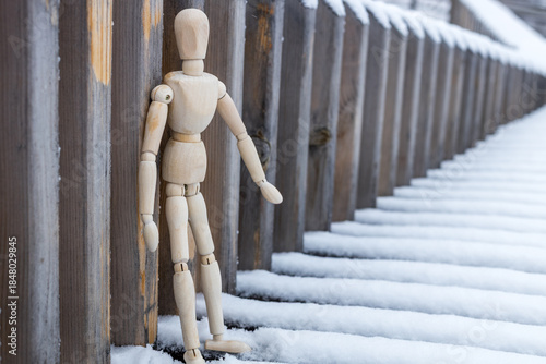 A wooden figure is standing in the snow next to a wooden fence