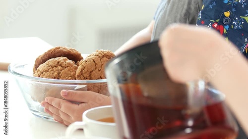 Child hands pours fruit tea in front of hands of girl holding homemade cookies